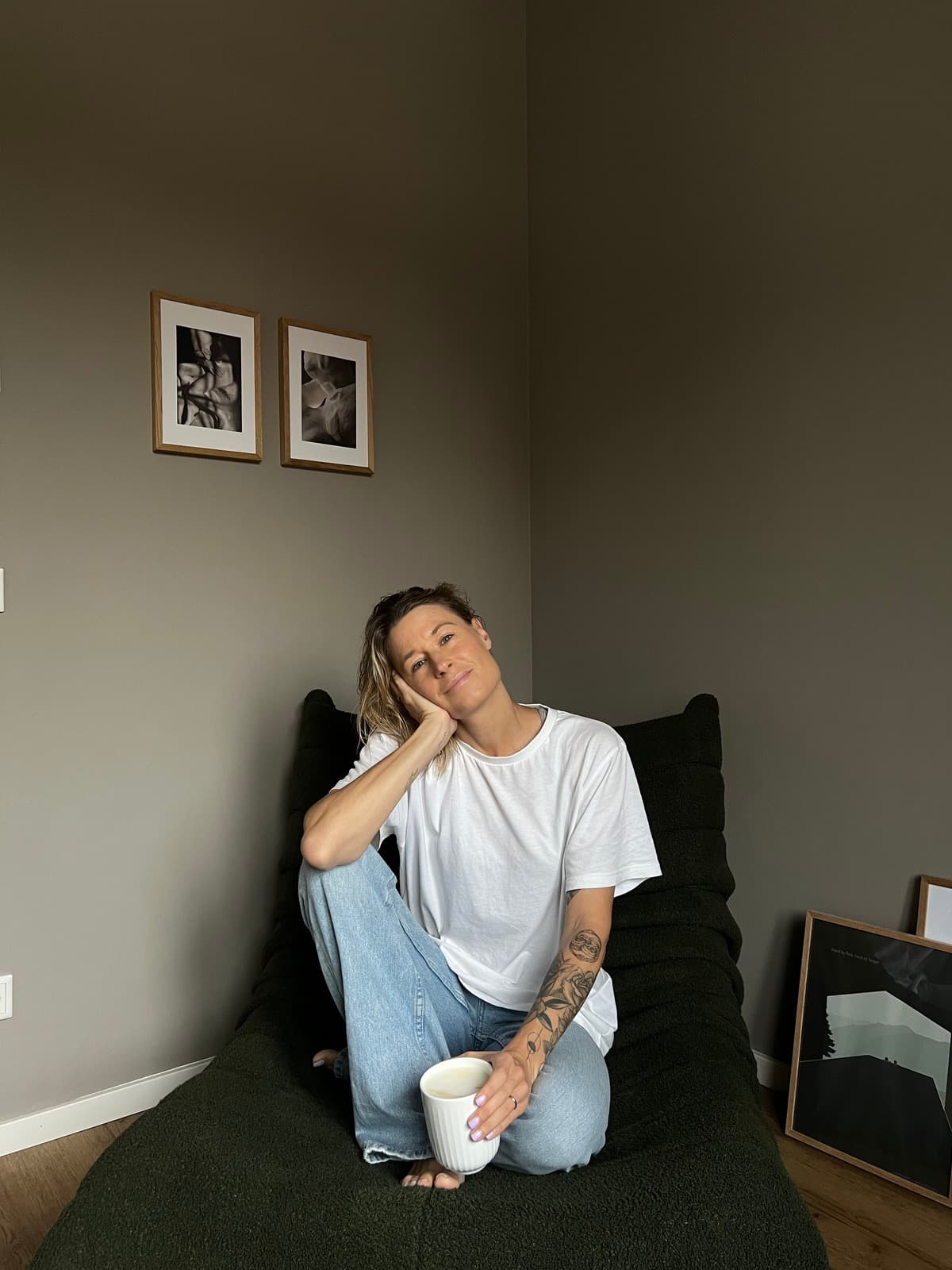 Sabrina sitzt mit einer Kaffeetasse auf einem dunkelgrünen Sessel an einer olivfarbenen Wand