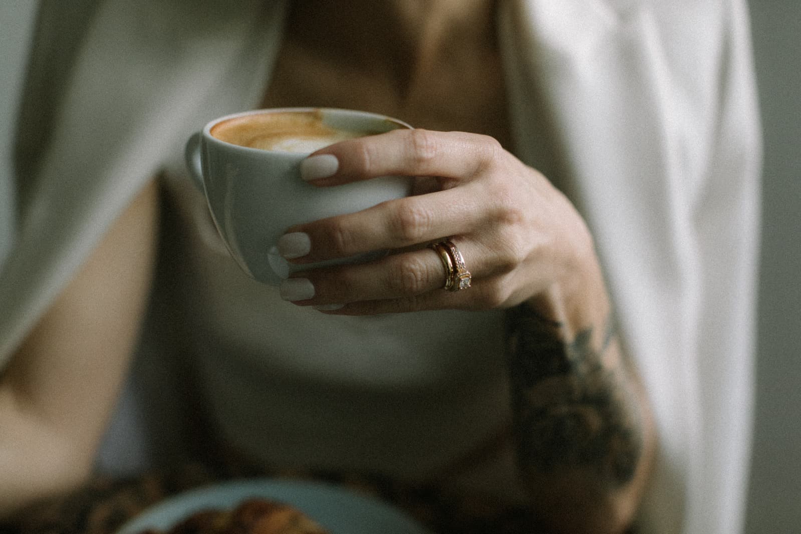 Hände halten eine Tasse Kaffee, im Hintergrund helle Kleidung