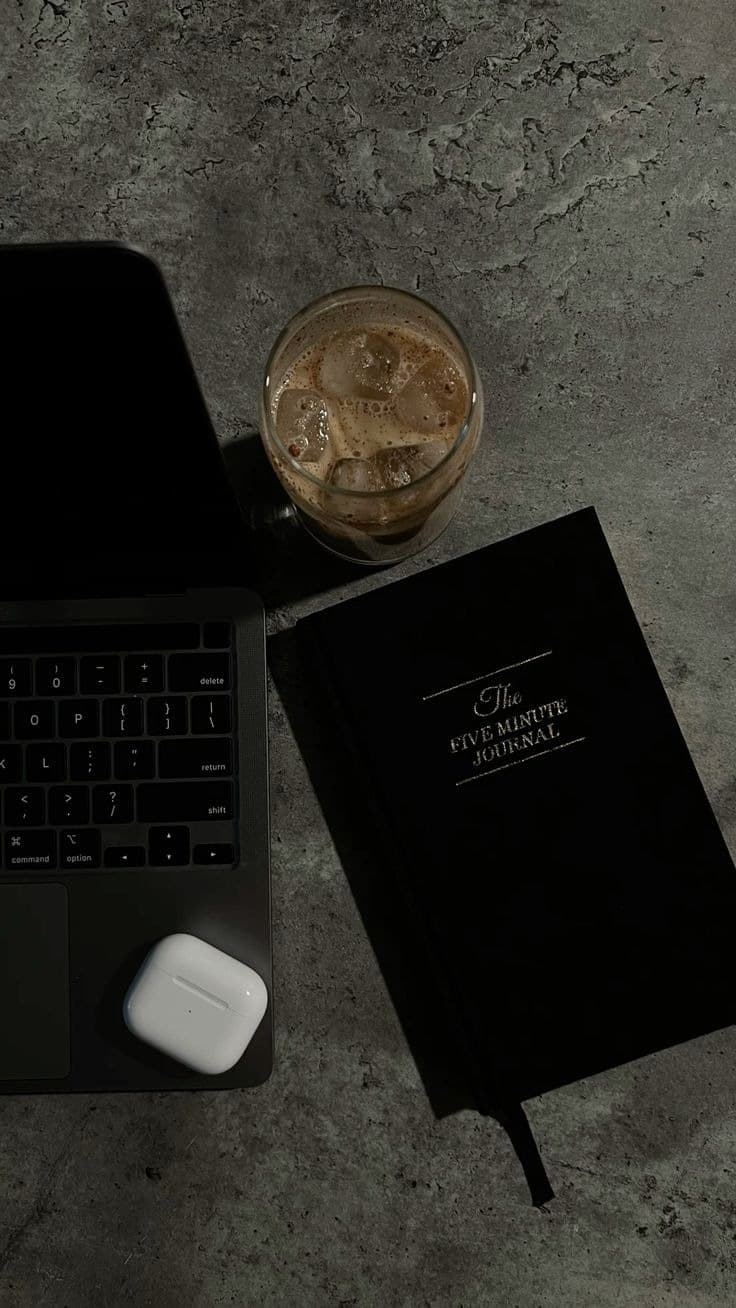 Laptop, Notizbuch und Eiskaffee auf einer Steinplatte, von oben fotografiert