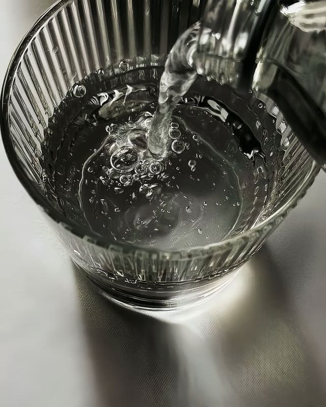 Wasser, das aus einer Karaffe in ein geripptes Glas gegossen wird