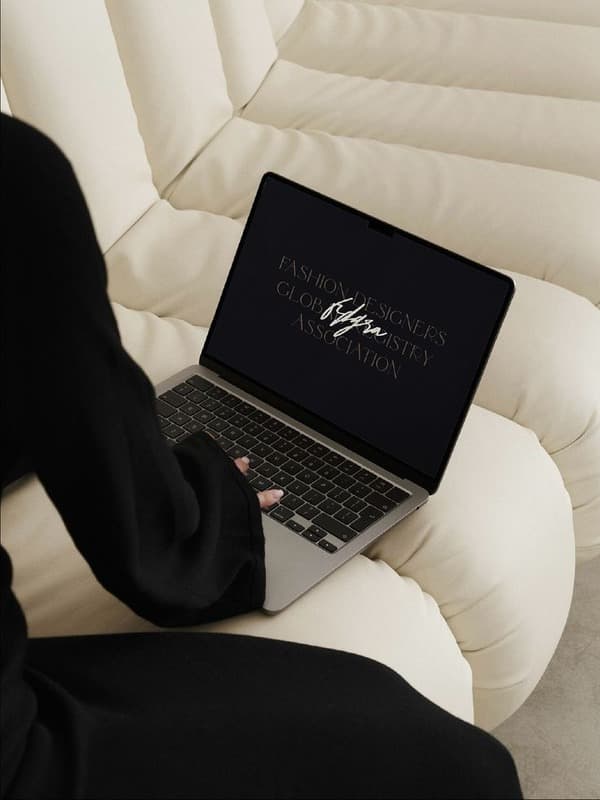 Person in Schwarz mit aufgeklapptem Laptop auf einem hellen Sessel